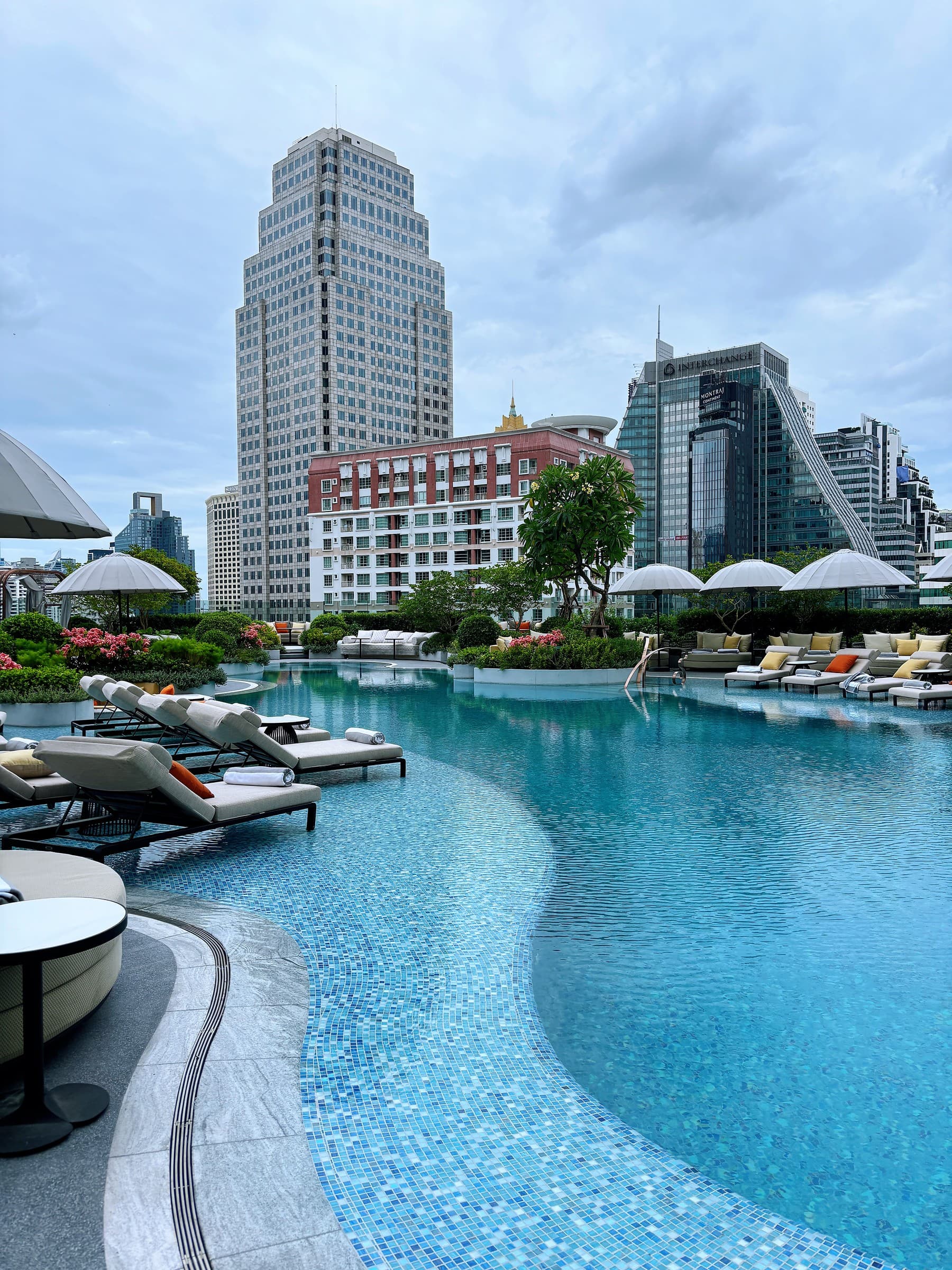 Fairmont Bangkok’s curved pool, loungers and parasols against the city skyline